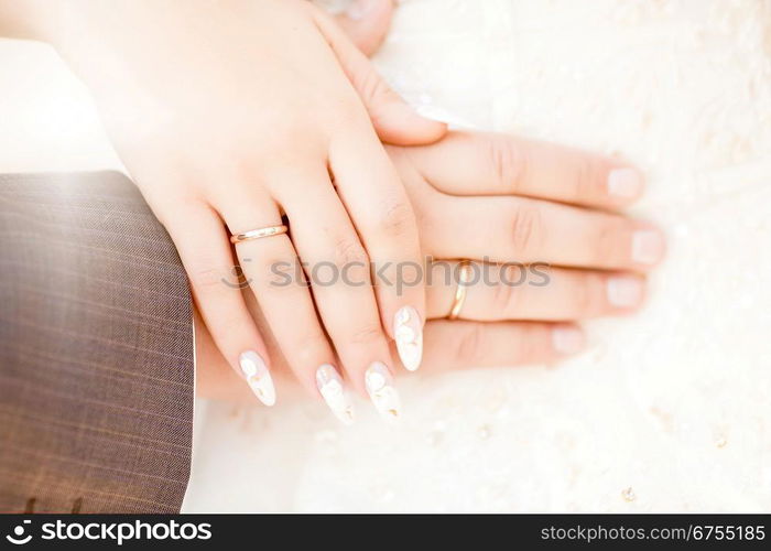 Loving couple holding hands with rings against wedding dress