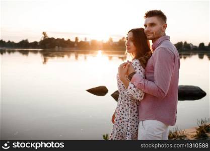 loving couple hugging on the lake at sunset. Beautiful young couple in love walking on the shore of the lake at sunset in the rays of bright light. copy space.. loving couple hugging on the lake at sunset. Beautiful young couple in love walking on the shore of the lake at sunset in the rays of bright light. copy space