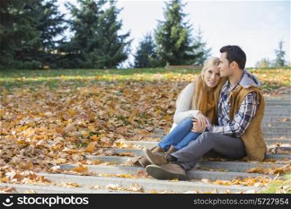 Loving couple hugging while sitting on steps in park during autumn