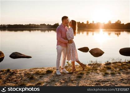 loving couple kissing on the lake at sunset. Beautiful young couple in love walking on the shore of the lake at sunset in the rays of bright light. copy space. loving couple kissing on the lake at sunset. Beautiful young couple in love walking on the shore of the lake at sunset in the rays of bright light. copy space.