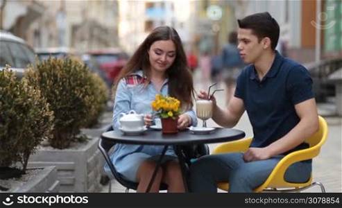 Loving couple relaxing in sidewalk cafe during romantic date. Romantic couple enjoying time together in coffee shop, chatting and drinking hot fresh coffee and tea on summer day.