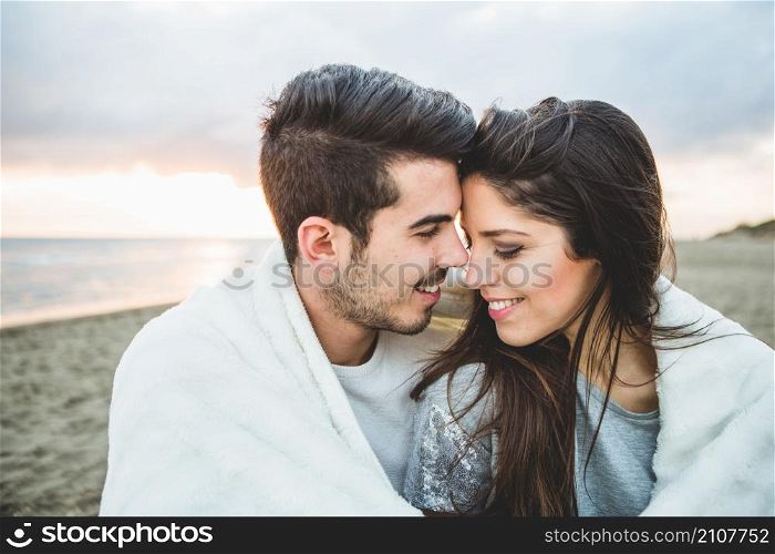 loving couple sitting beach covered by white blanket