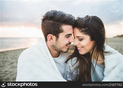 loving couple sitting beach covered by white blanket