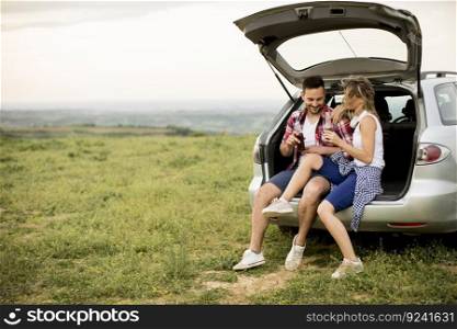 Loving couple sitting in the car trank during trip in the nature