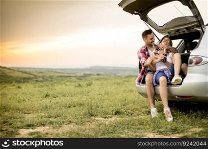 Loving couple sitting in the car trank during trip in the nature