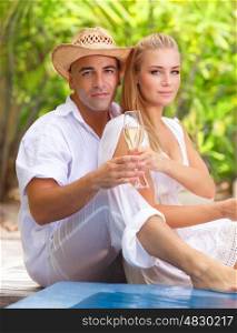 Loving couple sitting on the beach, drinking champagne on romantic tropical resort, spending happy summer holidays together