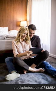 Loving couple sitting on the floor in bedroom and using digital tablet