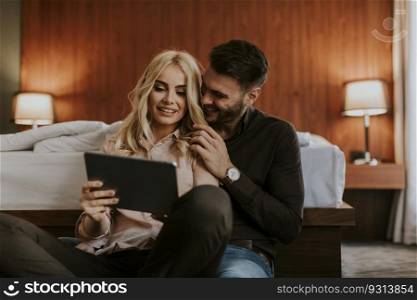 Loving couple sitting on the floor in bedroom and using digital tablet