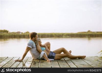 Loving couple sitting on the pier on lake at summer sunset