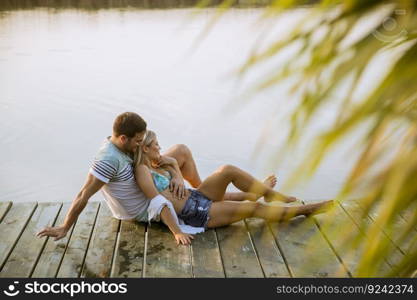 Loving couple sitting on the pier on lake at summer sunset