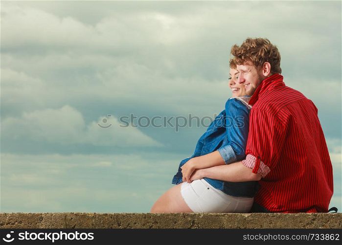 Loving couple spending leisure time together at beach sitting on sea shore hugging side view
