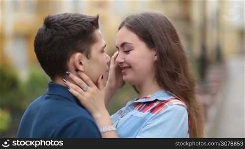Loving couple standing face to face, embracing, caressing and flirting with each other outdoors during romantic date. Portrait of passionate couple looking at camera with radiant toothy smile.