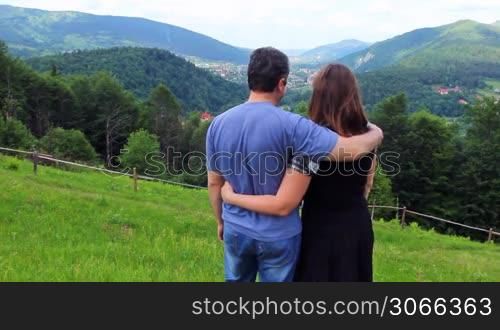 loving couple stands embracing on top of mountain and looks at beautiful view