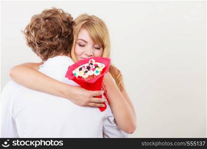 Loving couple with candy bunch bouquet flowers hugging. Pretty woman thanking man for present gift. Love concept.. Couple with candy bunch flowers hugging. Love.