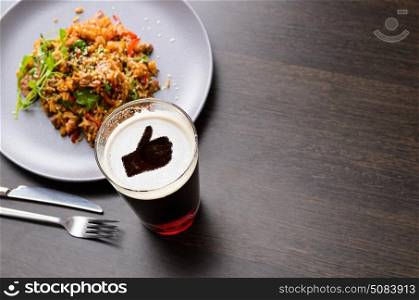 Loving dinner with beer. Thumbs up silhouette on foam in beer glass on black table with food, view from above.
