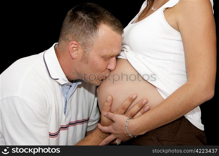 Loving father kissing the belly of his pregnant wife. Closeup over black