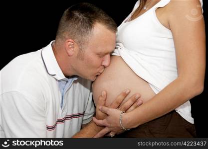 Loving father kissing the belly of his pregnant wife. Closeup over black
