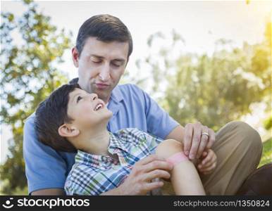 Loving Father Puts a Bandage on the Knee of His Young Son in the Park.