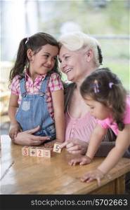 Loving grandmother teaching calculation to granddaughters at table in house