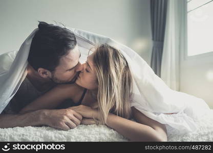 Loving happy couple in love smile and kiss each other under blanket on the bed, in big bedroom, Love story concept