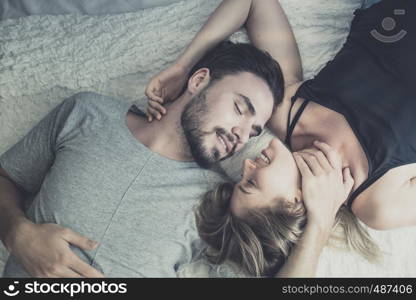 Loving happy couple in love smile and kiss her cheek on the bed, in big bedroom, Love story concept