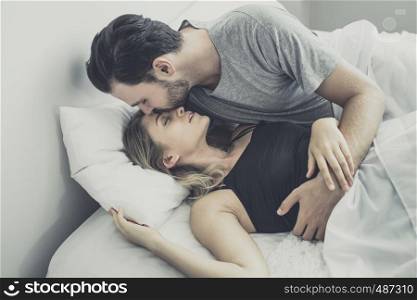 Loving happy couple in love smile, man kiss woman at forhead for wake her up on the bed, in morning, Love story concept