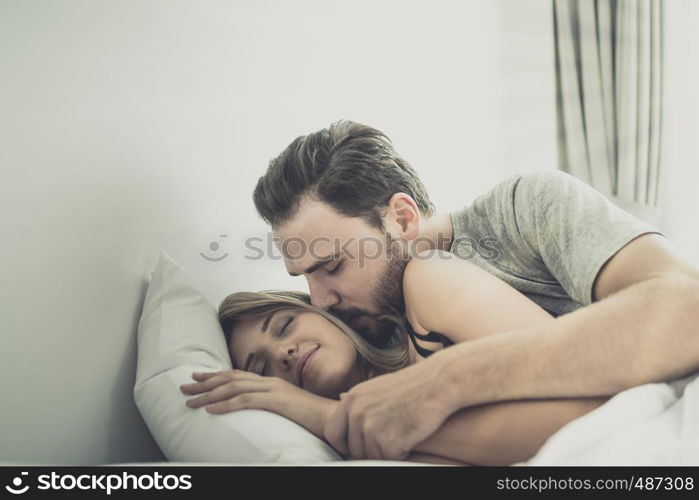 Loving happy couple in love smile, man kiss woman on cheek for wake her up on the bed, in morning, Love story concept