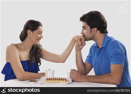 Loving man kissing woman on hand while having coffee against white background