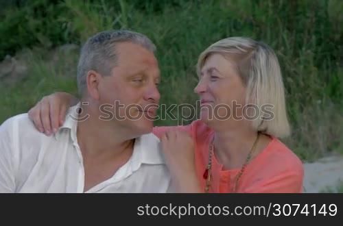 Loving mature couple outdoor. They looking into distance close to other, woman embracing mans over shoulders. Always together