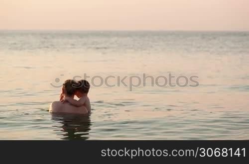 Loving mother and her young child bathing in the sea water by the beach in the sunset