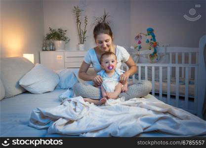 Loving mother changing diapers to her baby son on bed at night