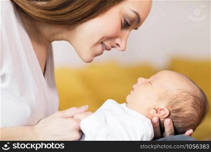 Loving Mother Cuddling Sleeping Baby Son On Lap At Home