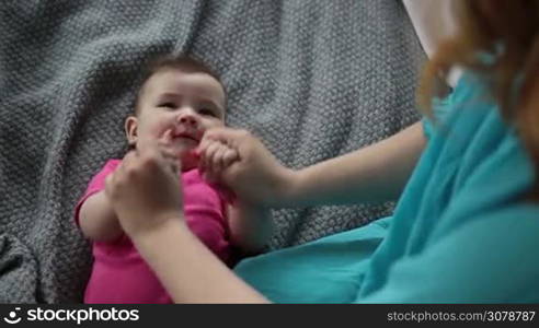 Loving mother doing gymnastic to laughing baby girl. Affectionate young mom massaging her lovely infant child. Top view. Shot over shoulder. Slow motion. Early development and health care concept.