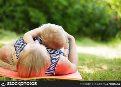 Loving mother hugging her little baby lying on green grass lawn. Relax on nature