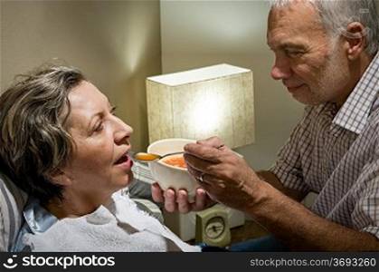 Loving retired husband feeding his ill wife with soup