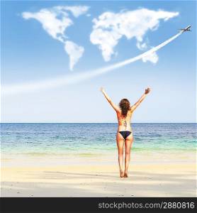loving travelling. young woman on beach is trying to embrace continents shaped clouds