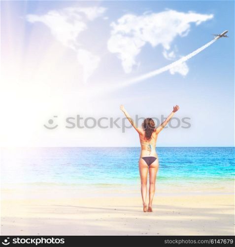 loving travelling. young woman on beach is trying to embrace continents shaped clouds. loving travelling concept