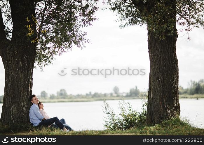 Loving young couple are hugging and smiling outdoors near the lake on sunny day. Love and tenderness, dating, romance, family concept. Loving young couple are hugging and smiling outdoors near the lake on sunny day. Love and tenderness, dating, romance, family concept.