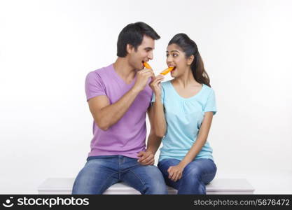 Loving young couple eating ice lollies on bench isolated over white background