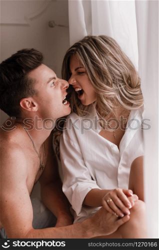 loving young couple enjoying morning at home near the window on Valentine&rsquo;s Day. girl in white shirt and guy half naked having fun together.. loving young couple enjoying morning at home near the window on Valentine&rsquo;s Day. girl in white shirt and guy half naked having fun together