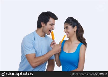 Loving young couple feeding each other ice lollies over white background