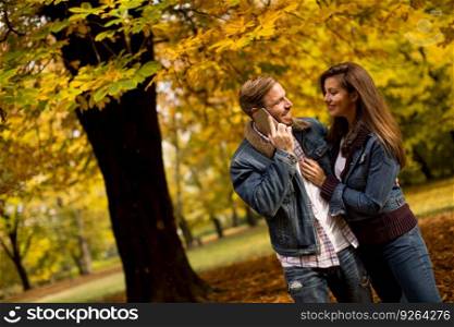 Loving young couple in the autumn park and man talking over the phone