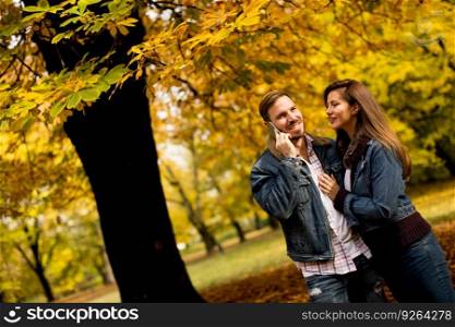 Loving young couple in the autumn park and man talking over the phone