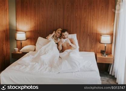 Loving young couple lying in the bedroom with mobile phone