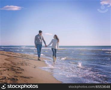 Loving young couple on a beach at autumn sunny day. Young couple having fun walking and hugging on beach during autumn sunny day colored filter
