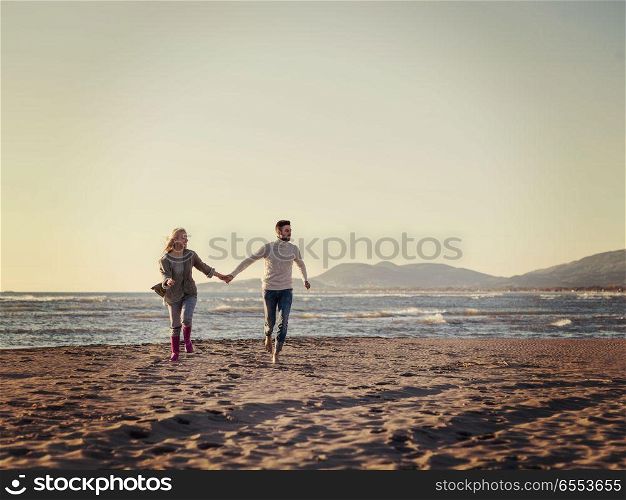 Loving young couple on a beach at autumn sunny day. Young couple having fun walking and hugging on beach during autumn sunny day colored filter