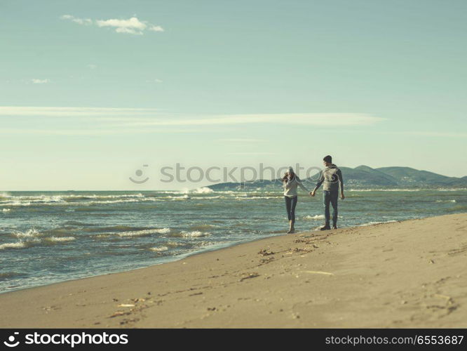 Loving young couple on a beach at autumn sunny day. Young couple having fun walking and hugging on beach during autumn sunny day colored filter