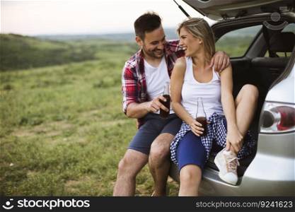 Loving young couple sitting in the car trank during trip in the nature