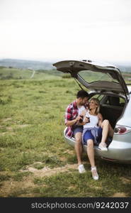 Loving young couple sitting in the car trank during trip in the nature