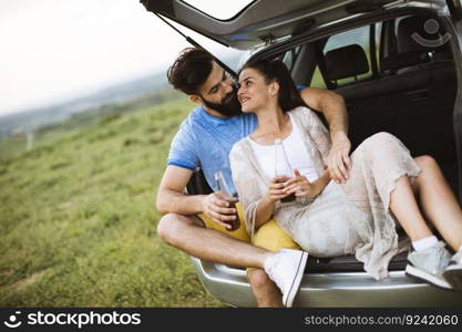 Loving young couple sitting in the car trank during trip in the nature